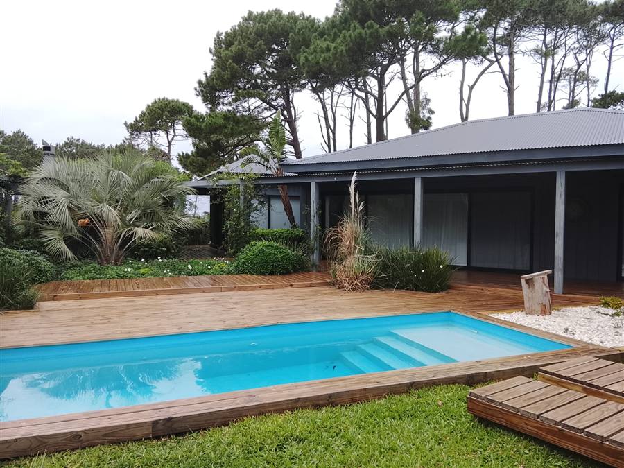 Casa con pileta rodeada de deck de madera recién pintado y jardín