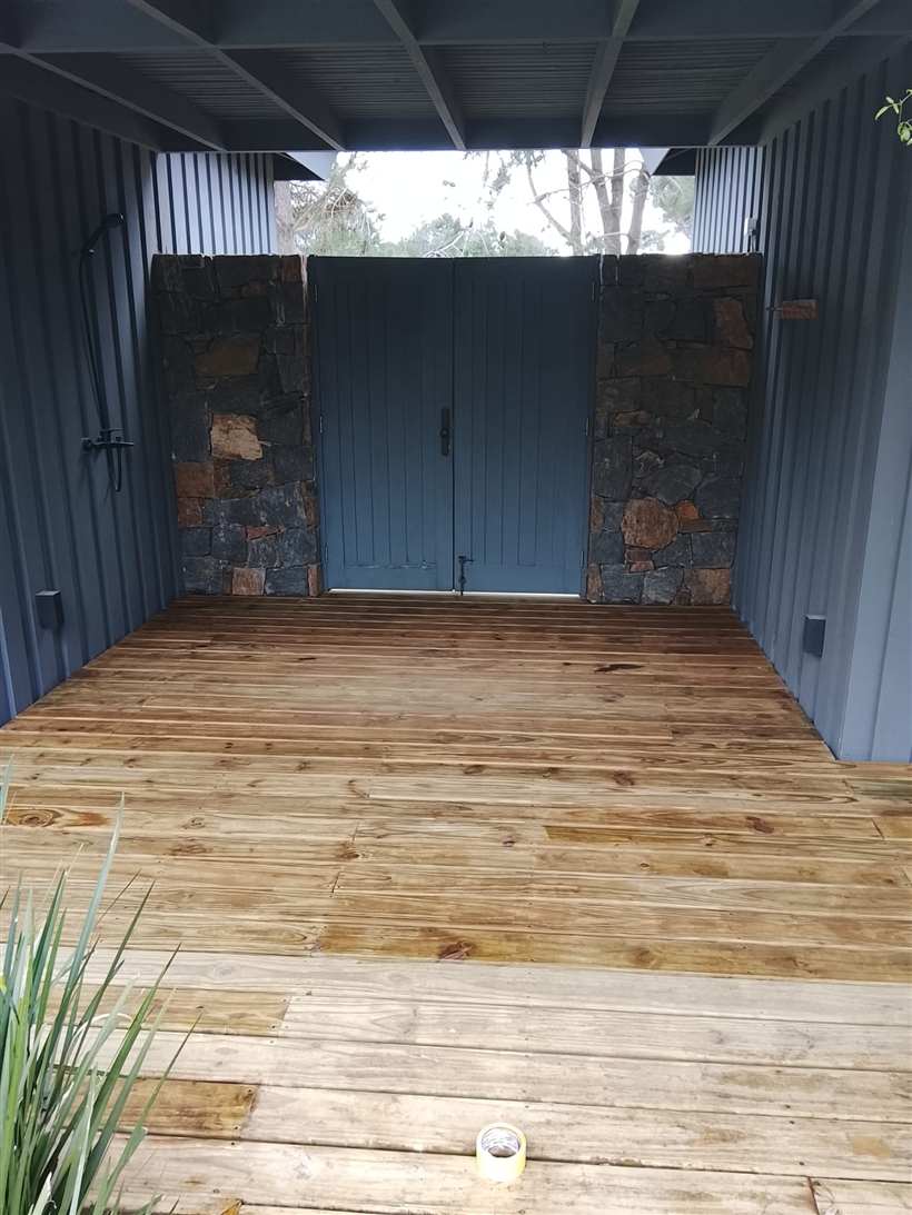 Ducha exterior con muros de piedra y portón de madera, con el deck pintado