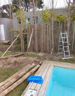 Postes y troncos de madera listos al pie de una obra de Hornero